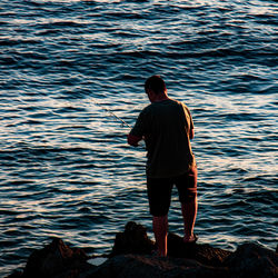 Rear view of man standing on rock in sea