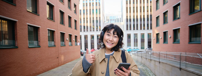 Portrait of young woman standing against building