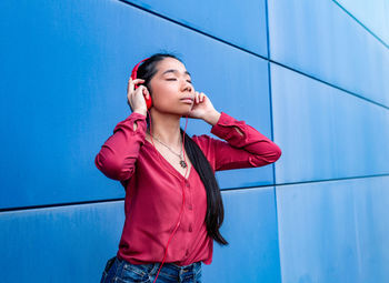 Young woman looking away while standing against blue wall