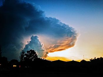 Silhouette smoke emitting from building against sky at sunset