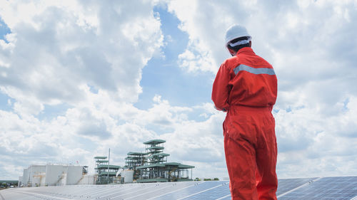 Engineer standing amidst solar panel against cloudy sky