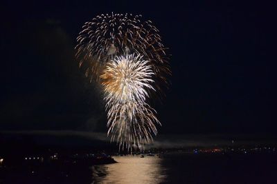 Firework display over sea against sky at night