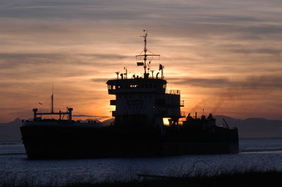Silhouette ship in sea against orange sky