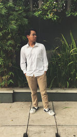 Full length of young man looking away while standing against plants