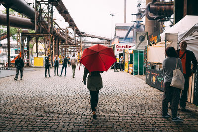 Rear view of woman carrying umbrella while walking on cobblestone street