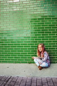 Portrait of woman sitting against brick wall