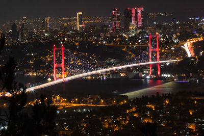 Illuminated bridge and buildings against sky at night