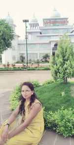 Portrait of smiling woman sitting on plant against building