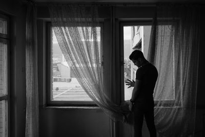 Side view of man standing by window at home