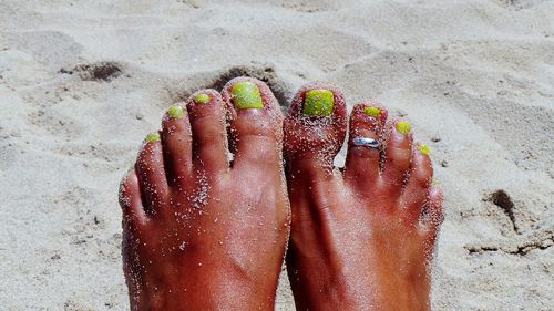 Low section of woman with toe ring resting on sand at beach