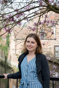 Smiling beautiful young girl stands on the old bridge under blossoming trees