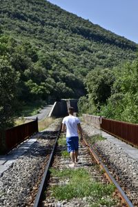 Rear view of man walking on railroad track