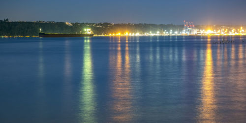 Illuminated city by river against sky at night