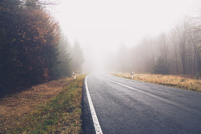 Empty road amidst trees against sky