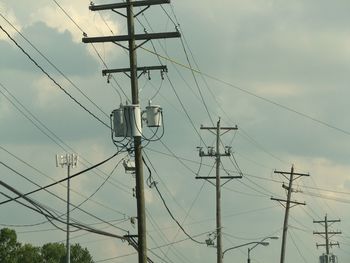 Low angle view of electricity pylon against cloudy sky