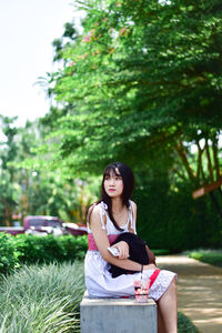 Portrait of woman sitting on plant against trees