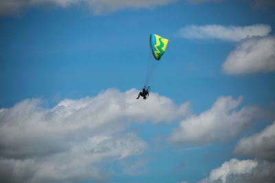 Low angle view of people paragliding against sky