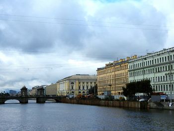 View of canal with bridge in city against cloudy sky