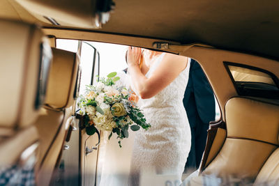 Midsection of bride with bouquet standing by car