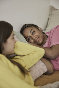 Smiling teenage girl resting on bed with female friend in bedroom at home