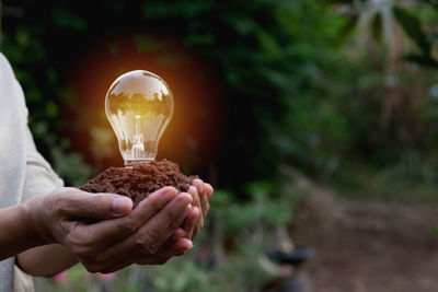 Close-up of hand holding mud and illuminated light bulb