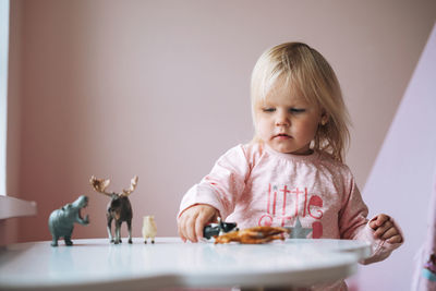 Little girl toddler in pink playing with animal toys on table in children's room at home