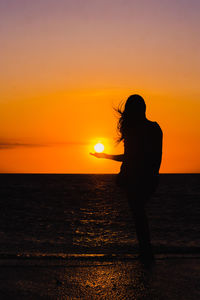 Silhouette woman on beach against sky during sunset