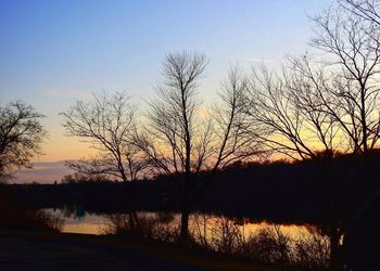 Silhouette bare trees by lake against sky during sunset