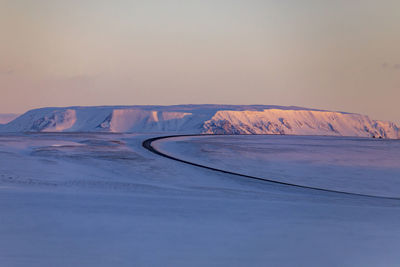 Empty winding asphalt roadway leading through valley covered with snow in highlands during sunset in winter in iceland