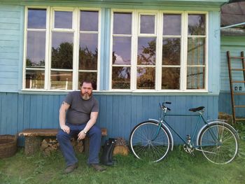 Full length portrait of smiling man on bicycle against building