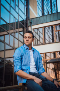 Young man looking away while sitting on railing