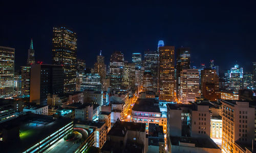 Illuminated modern buildings in city against sky at night