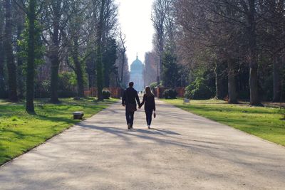 Rear view of couple walking on road along amidst park