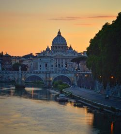 Bridge over river against buildings in city at sunset