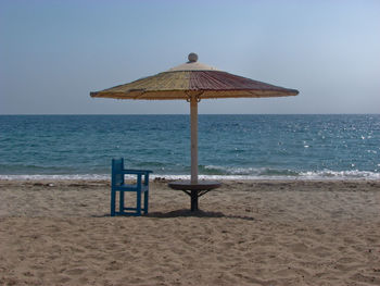 Thatched umbrella and chair on beach against clear sky