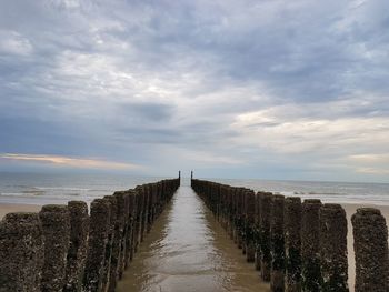 Wooden posts on sea against sky