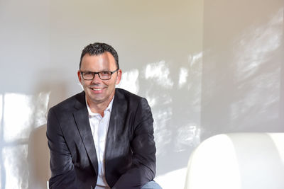 Portrait of businessman sitting on sofa against white wall