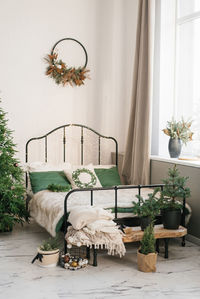 Bed with a beige plaid and green pillows, a christmas wreath on the wall, a christmas tree