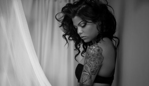 Side view of seductive woman with tattoo against curtain