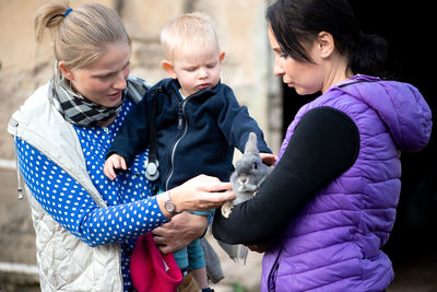 Mother with son looking at rabbit being held by woman in park