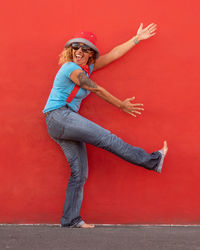 Full length portrait of mature woman dancing by red wall