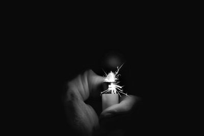 Cropped hand igniting cigarette lighter in darkroom