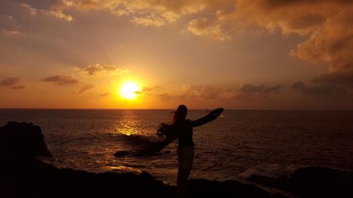 Silhouette person standing on beach against sky during sunset