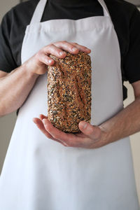 Close-up at bakers hands holding a multi-seeded loaf of sourdough whole grain bread in front of him.