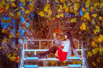 Young woman sitting on bleachers against trees