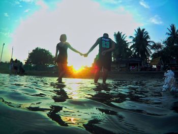 People swimming in pool against sky during sunset