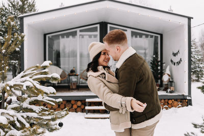 A couple in love in warm clothes walk against the background of a country house in a winter forest