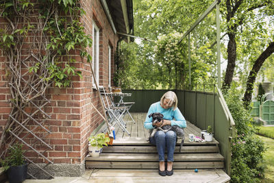 Happy woman sitting with dog on steps outside house