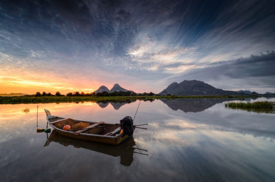 Boat moored on lake against sky during sunset