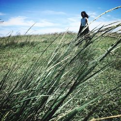 Young woman walking on grassy field against sky during sunny day